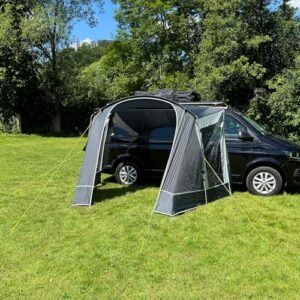 Freizeitschmiede CaliShade Sonnensegel für Busse und Vans, montiert an einem schwarzen Fahrzeug auf einer Wiese, mit grauem Material und offenen Seiten für Belüftung.