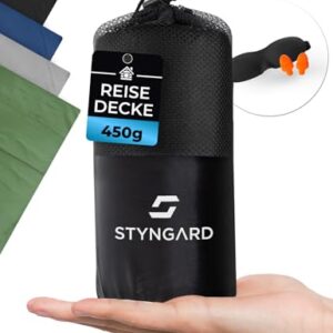 Kompakte Reisedecke aus Fleece in einem schwarzen Packbeutel, ideal für Reisen, Camping und Outdoor-Aktivitäten, inklusive Ohrstöpseln als Zubehör.