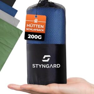 Kompakter Hüttenschlafsack aus Mikrofaser in blauer Tasche, die von einer Hand gehalten wird, ideal für Reisen und Camping.