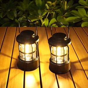 Zwei tragbare LED Campinglampen auf einem Holztisch, die warmes Licht ausstrahlen und eine gemütliche Atmosphäre im Freien schaffen. Ideal für Camping, Wandern und Notfälle.
