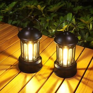 Zwei tragbare LED Campinglampen im klassischen Design auf einem Holzttisch, ideal für Camping und Notfälle, mit warmem Licht und IPX4 wasserdichter Bauweise.