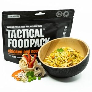 Tactical Foodpack Nudeln mit Hähnchen-Kokos-Sauce in schwarzer Verpackung mit frischen Gemüsestückchen in Holzschale, ideal für Outdoor und Notfallsituationen