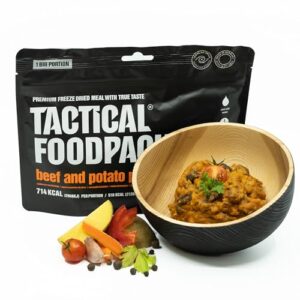 Tactical Foodpack Rindfleischeintopf mit Kartoffeln in schwarzer Schüssel, umgeben von frischen Zutaten auf einem modernen Hintergrund.