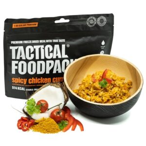 Tactical Foodpack Scharfes Hähnchen-Curry 120g in einer Schüssel, umgeben von frischen Zutaten wie Chilischoten und Kräutern, mit einer schwarzen Verpackung im Hintergrund.